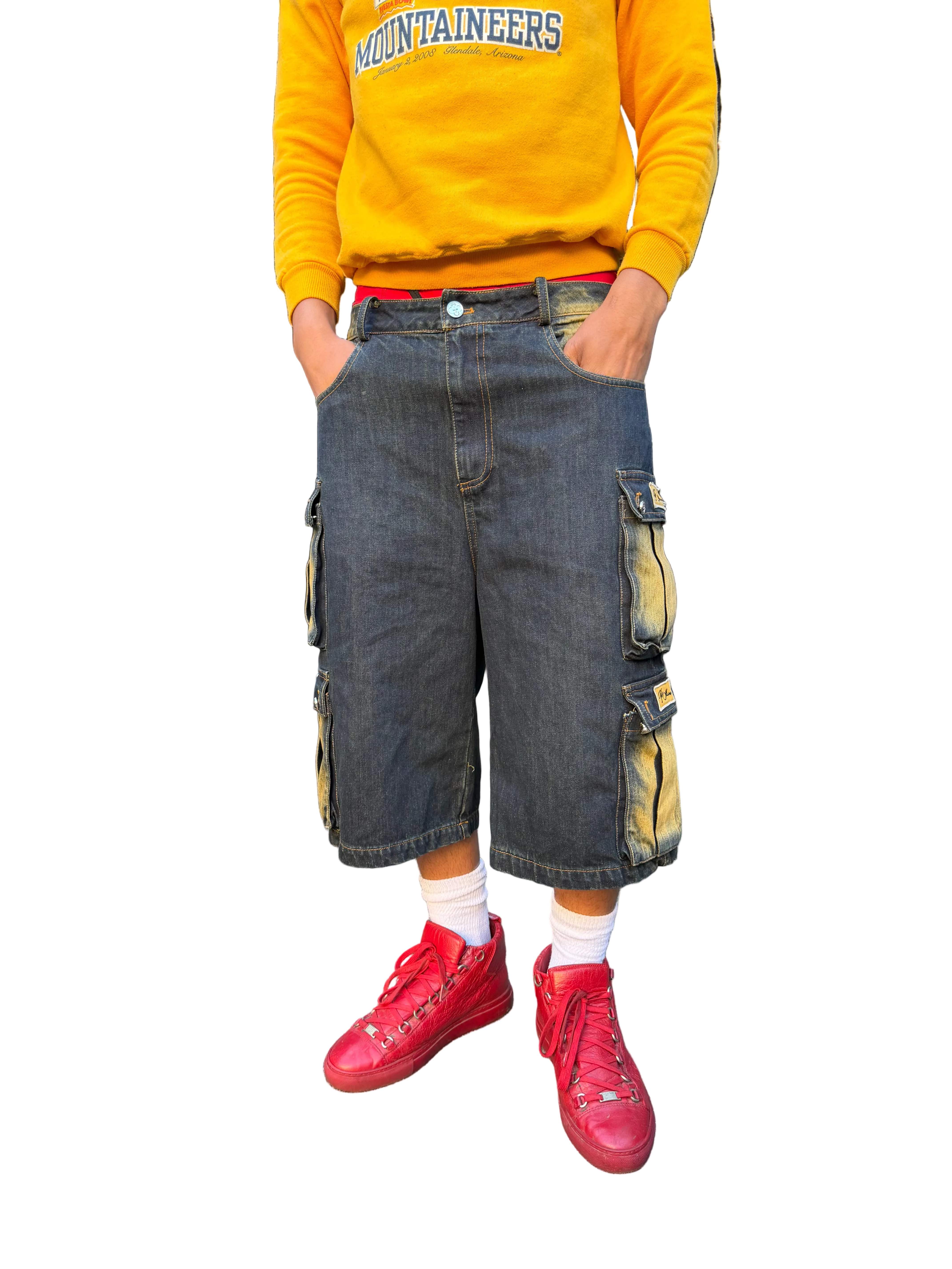 Person wearing a yellow sweatshirt with 'Mountaineers' text, dark cargo shorts, and red sneakers in a parking lot.